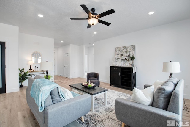 living room with light hardwood / wood-style flooring, ceiling fan, and a textured ceiling