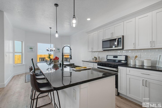 kitchen with appliances with stainless steel finishes, light wood-type flooring, a wealth of natural light, and an inviting chandelier