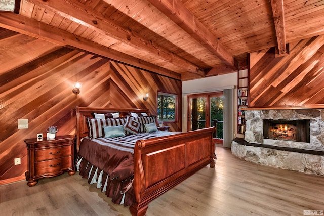 bedroom with light wood-type flooring, beamed ceiling, wood walls, a stone fireplace, and wooden ceiling