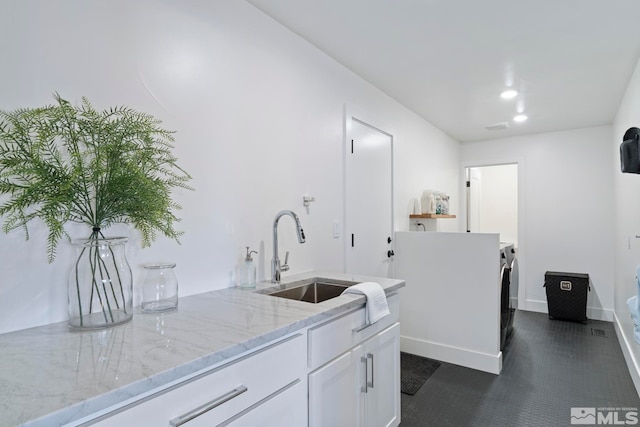 kitchen with dark tile floors, white cabinetry, sink, and light stone countertops