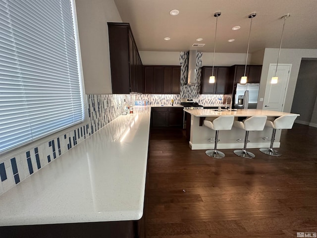 kitchen with hanging light fixtures, dark wood-type flooring, a kitchen bar, an island with sink, and stainless steel appliances