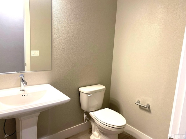 half bath featuring baseboards, a textured wall, a sink, and toilet