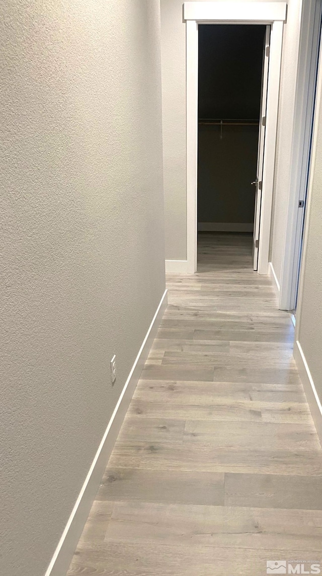hall featuring a textured wall, wood finished floors, and baseboards