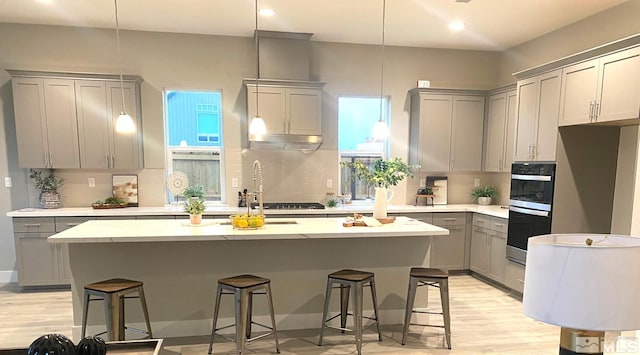 kitchen featuring stainless steel appliances, backsplash, gray cabinets, light wood finished floors, and an island with sink