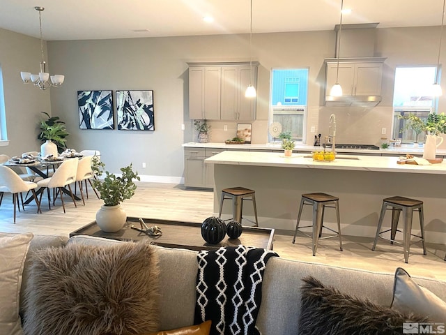 kitchen featuring gray cabinetry, light wood-style floors, a kitchen breakfast bar, tasteful backsplash, and pendant lighting