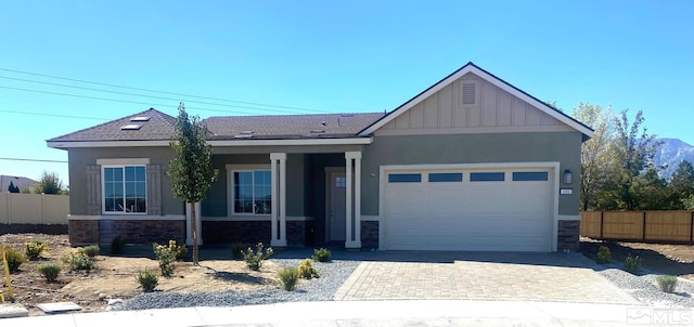 view of front of house featuring an attached garage, stone siding, fence, and board and batten siding