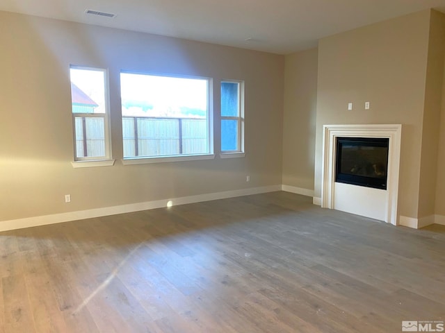 unfurnished living room with wood finished floors, a glass covered fireplace, visible vents, and baseboards