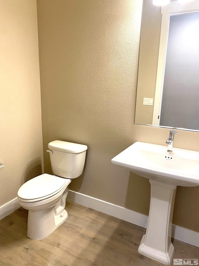 half bathroom with baseboards, toilet, and wood finished floors