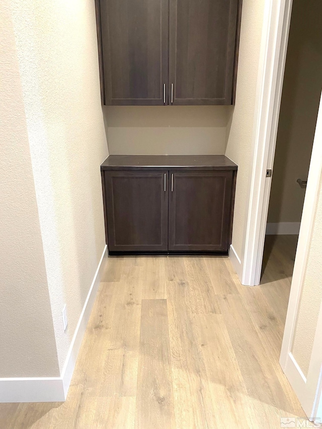 interior space featuring baseboards, a textured wall, and light wood-style floors