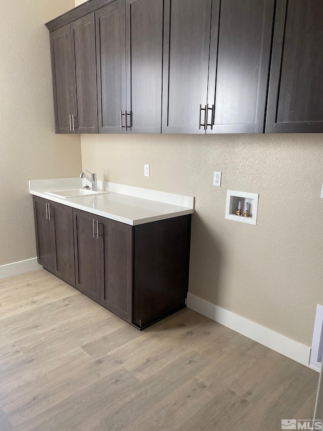 laundry room with cabinet space, baseboards, light wood-style floors, washer hookup, and a sink