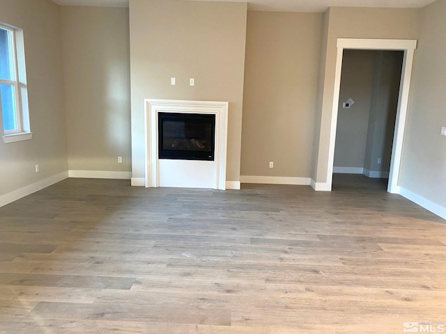 unfurnished living room featuring a glass covered fireplace, baseboards, and wood finished floors