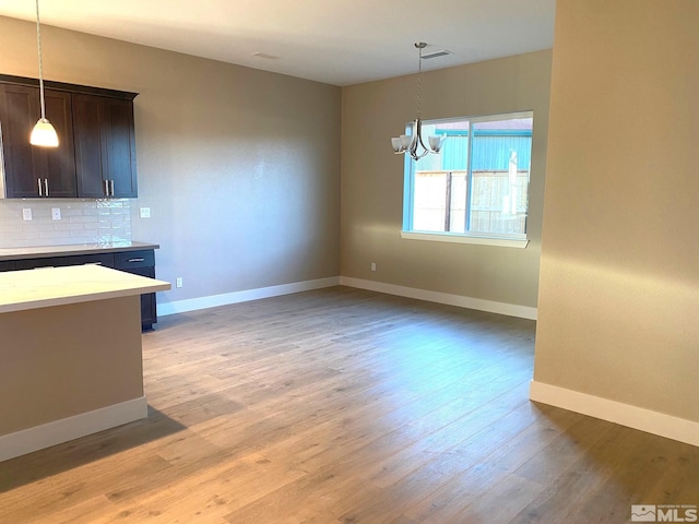 unfurnished dining area with a notable chandelier, light wood-style flooring, and baseboards