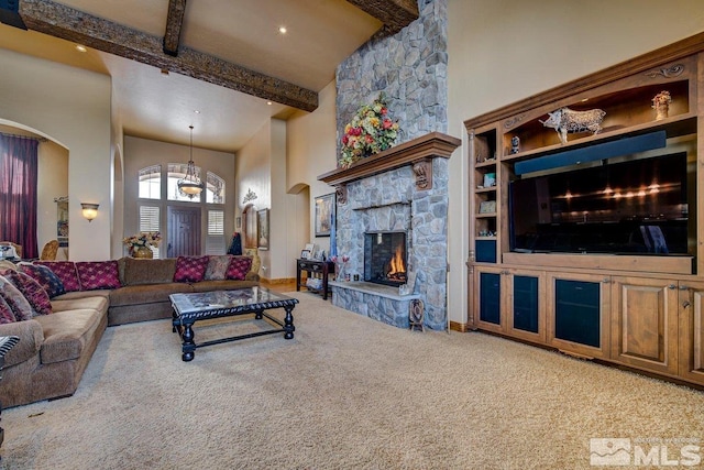 living room with light colored carpet, a towering ceiling, beamed ceiling, an inviting chandelier, and a stone fireplace