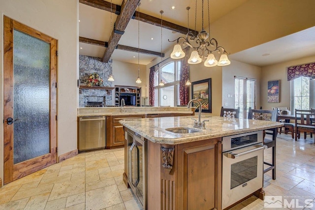 kitchen with stainless steel appliances, decorative light fixtures, beam ceiling, a kitchen island with sink, and sink