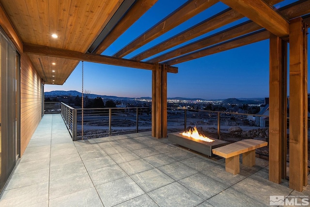 patio terrace at dusk with an outdoor fire pit, a mountain view, and a pergola