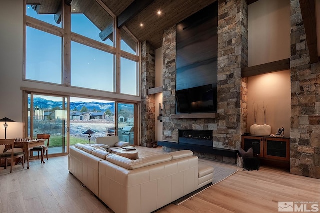 living room with beam ceiling, a mountain view, a stone fireplace, high vaulted ceiling, and light hardwood / wood-style flooring