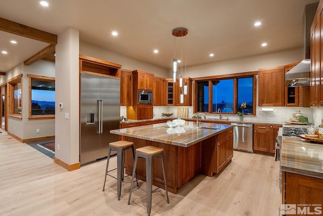 kitchen featuring built in appliances, backsplash, light hardwood / wood-style flooring, and an island with sink