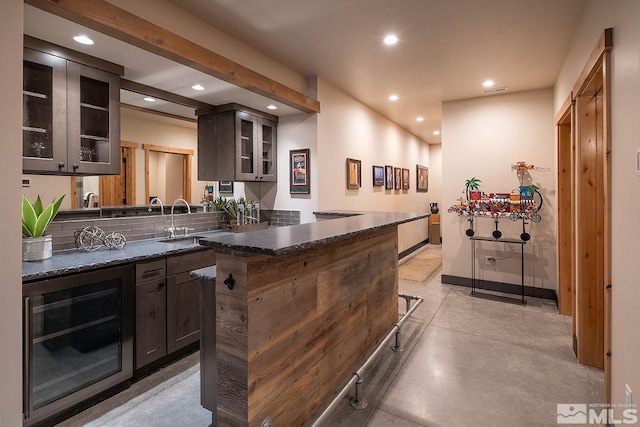 bar with sink, dark stone counters, tasteful backsplash, and dark brown cabinetry