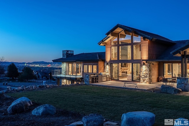 back house at dusk featuring a lawn, an outdoor kitchen, and a patio