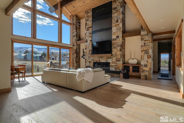 unfurnished living room featuring light hardwood / wood-style flooring, high vaulted ceiling, a fireplace, and beamed ceiling