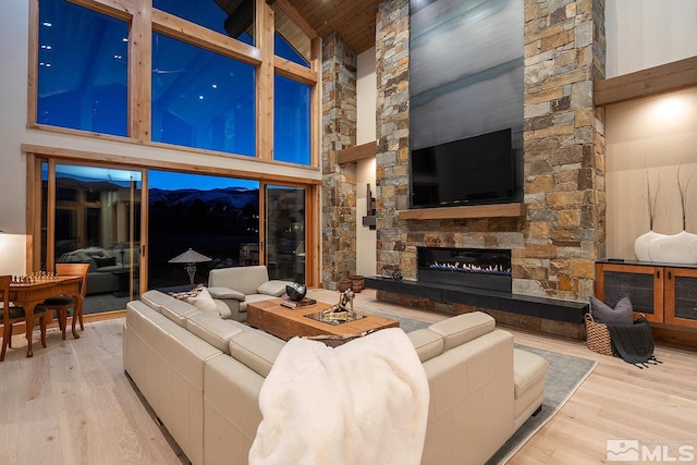 living room with high vaulted ceiling, a mountain view, light wood-type flooring, and a stone fireplace