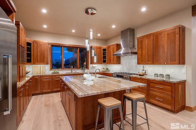 kitchen featuring backsplash, a breakfast bar, light hardwood / wood-style flooring, an island with sink, and wall chimney exhaust hood