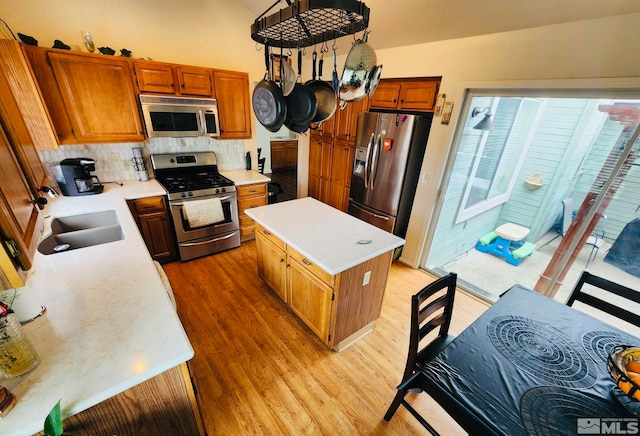 kitchen featuring a kitchen island, appliances with stainless steel finishes, backsplash, light wood-type flooring, and sink