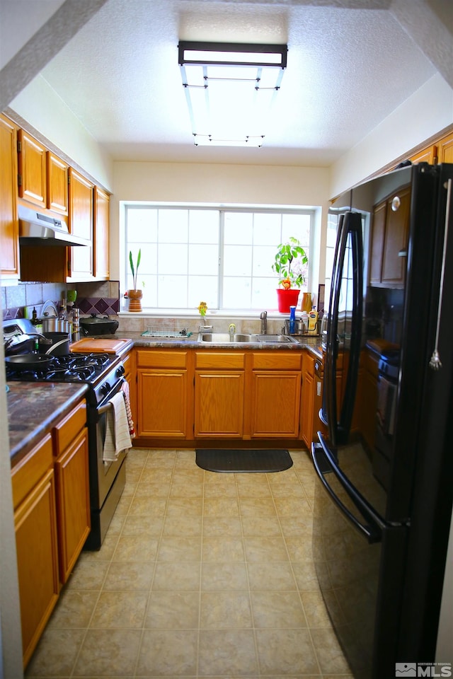 kitchen featuring backsplash, sink, black appliances, light tile patterned flooring, and a textured ceiling