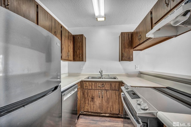 kitchen with appliances with stainless steel finishes, sink, dark hardwood / wood-style floors, and a textured ceiling