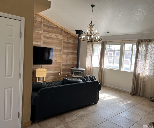 tiled living room with wood walls, a textured ceiling, a chandelier, and a wood stove