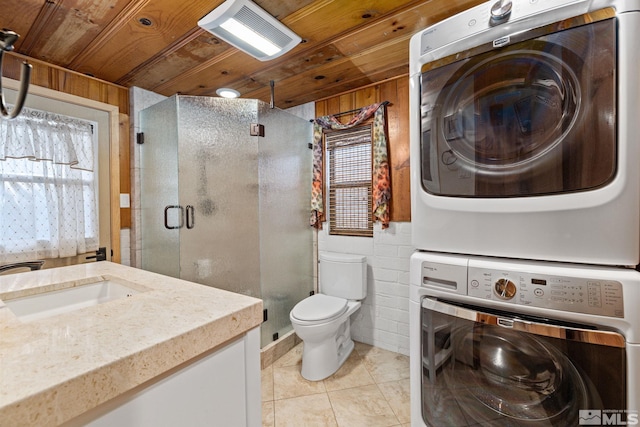 bathroom featuring stacked washing maching and dryer, tile patterned flooring, wooden walls, vanity, and wood ceiling