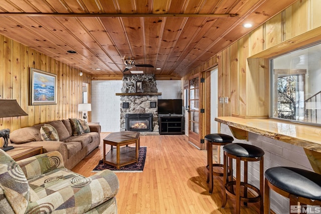 living room featuring a stone fireplace, light hardwood / wood-style flooring, wood walls, and wood ceiling