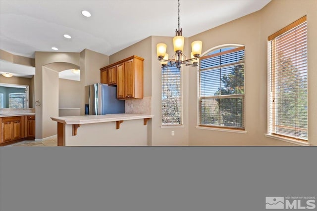 kitchen featuring decorative light fixtures, backsplash, stainless steel refrigerator with ice dispenser, a breakfast bar, and light tile flooring