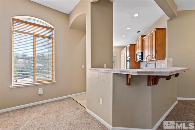 kitchen with light colored carpet, a kitchen breakfast bar, plenty of natural light, and tasteful backsplash