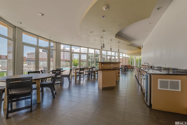 interior space featuring a wall of windows, sink, pendant lighting, and dark tile floors