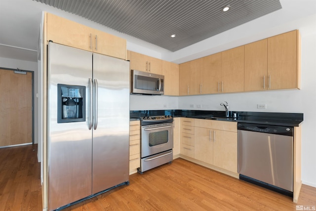 kitchen featuring a barn door, appliances with stainless steel finishes, light brown cabinetry, sink, and light wood-type flooring