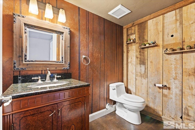 bathroom with wood walls, toilet, and vanity