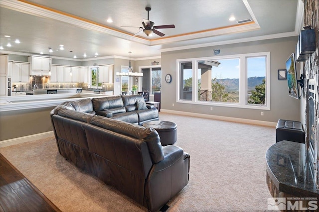 living room featuring ceiling fan with notable chandelier, a raised ceiling, light carpet, and ornamental molding