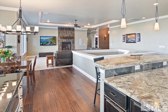 kitchen with pendant lighting, a stone fireplace, a kitchen breakfast bar, a raised ceiling, and dark hardwood / wood-style flooring