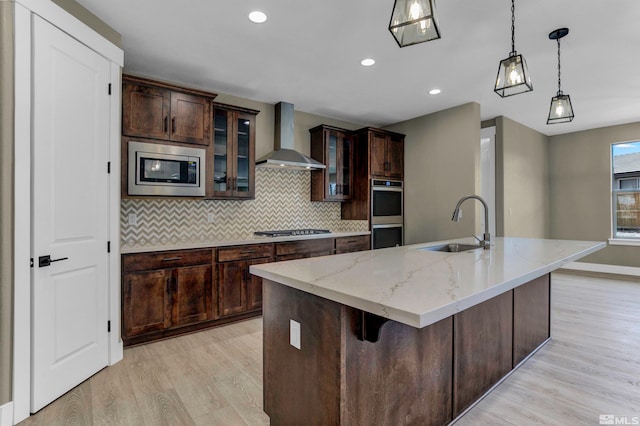 kitchen with appliances with stainless steel finishes, wall chimney exhaust hood, backsplash, decorative light fixtures, and light hardwood / wood-style flooring