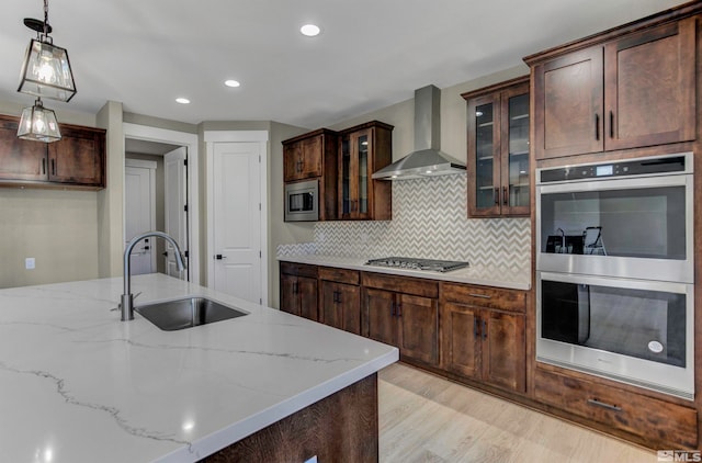 kitchen featuring backsplash, appliances with stainless steel finishes, wall chimney range hood, sink, and light hardwood / wood-style floors