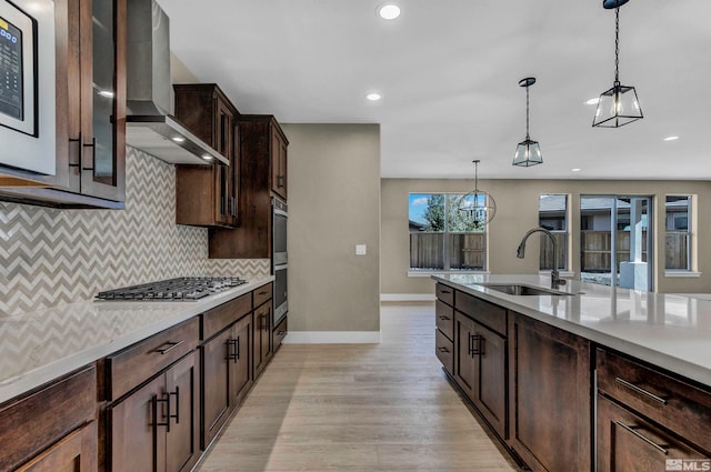 kitchen with backsplash, hanging light fixtures, stainless steel gas stovetop, light hardwood / wood-style floors, and wall chimney exhaust hood