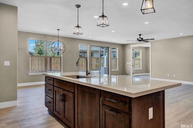 kitchen with decorative light fixtures, ceiling fan with notable chandelier, light hardwood / wood-style flooring, sink, and an island with sink