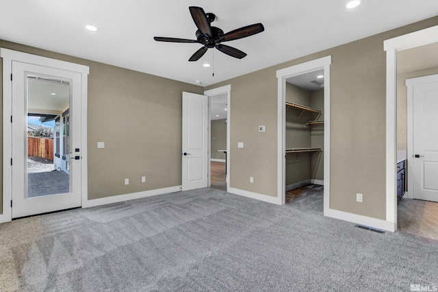 unfurnished bedroom with a closet, ceiling fan, a walk in closet, and light carpet