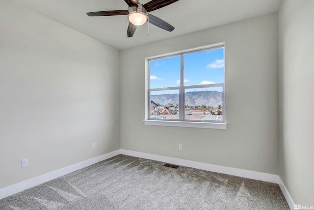 empty room with a mountain view, carpet flooring, and ceiling fan