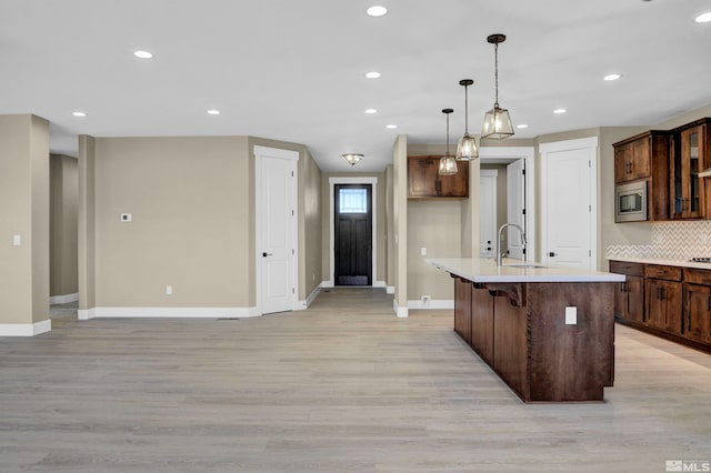 kitchen featuring a kitchen bar, hanging light fixtures, light wood-type flooring, and a kitchen island with sink