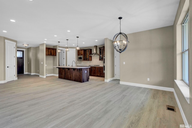 kitchen with plenty of natural light, hanging light fixtures, light hardwood / wood-style flooring, tasteful backsplash, and a kitchen island with sink