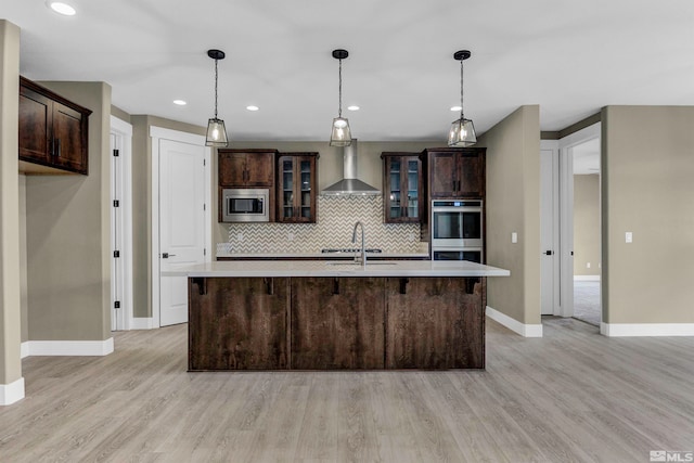 kitchen with appliances with stainless steel finishes, backsplash, a breakfast bar area, light hardwood / wood-style floors, and wall chimney exhaust hood