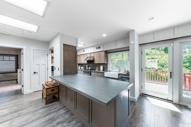 kitchen featuring stainless steel stove, a kitchen island, sink, light wood-type flooring, and dishwashing machine