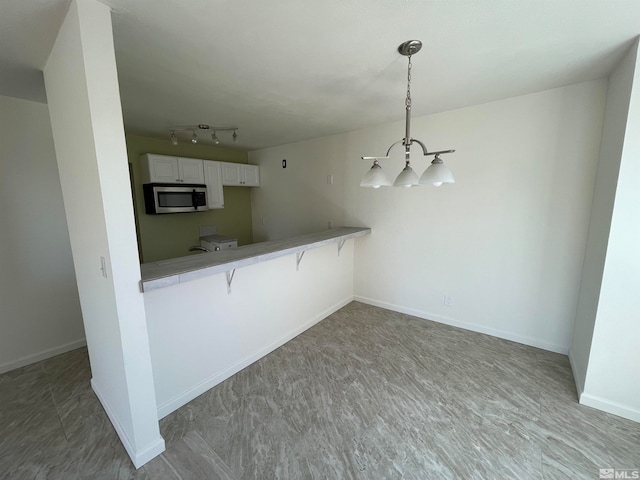 kitchen with white cabinets, kitchen peninsula, a breakfast bar area, pendant lighting, and an inviting chandelier